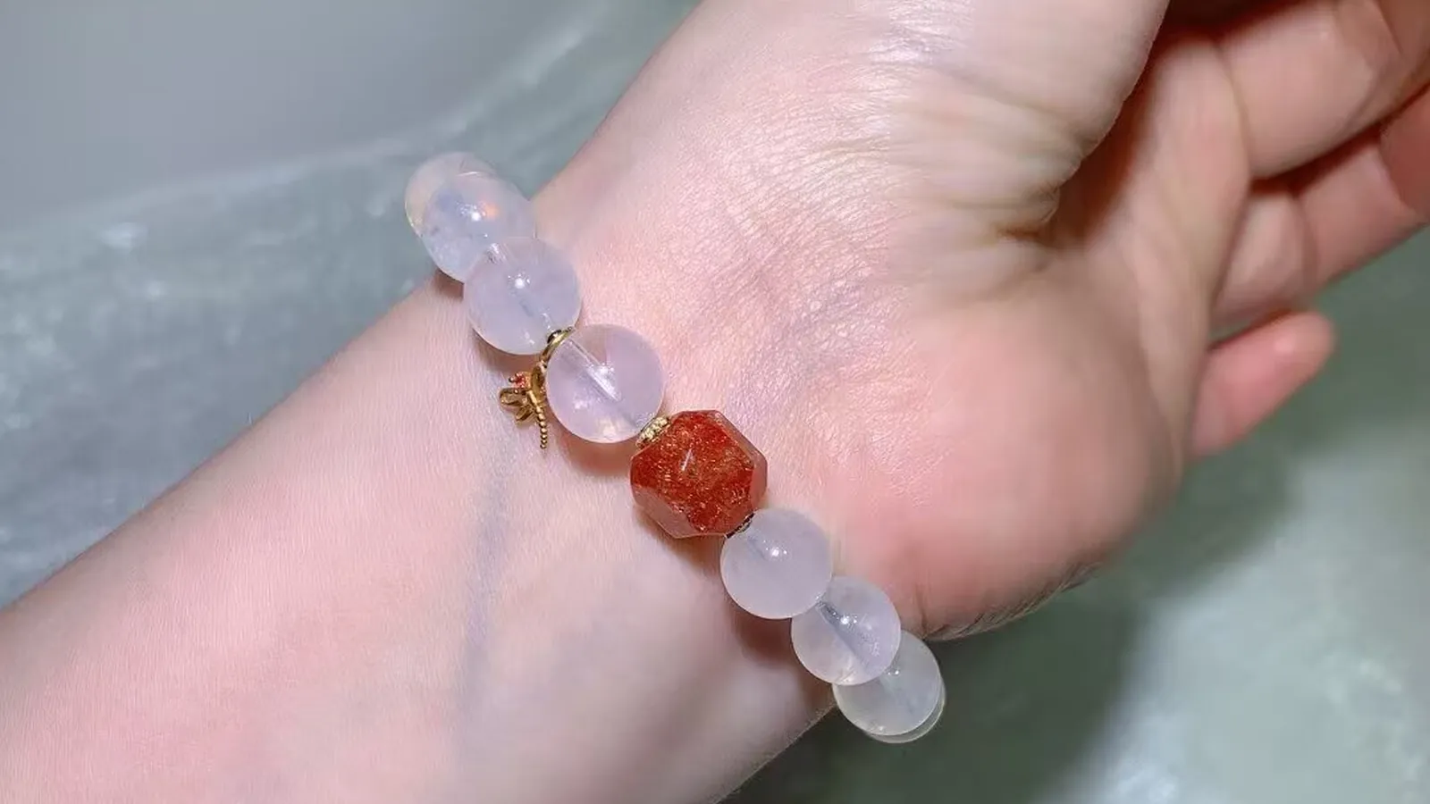 手腕上的蓝针水晶手链：冰透乳白色珠子，配一颗切面珊瑚橙色珠和小巧的古法饰品
