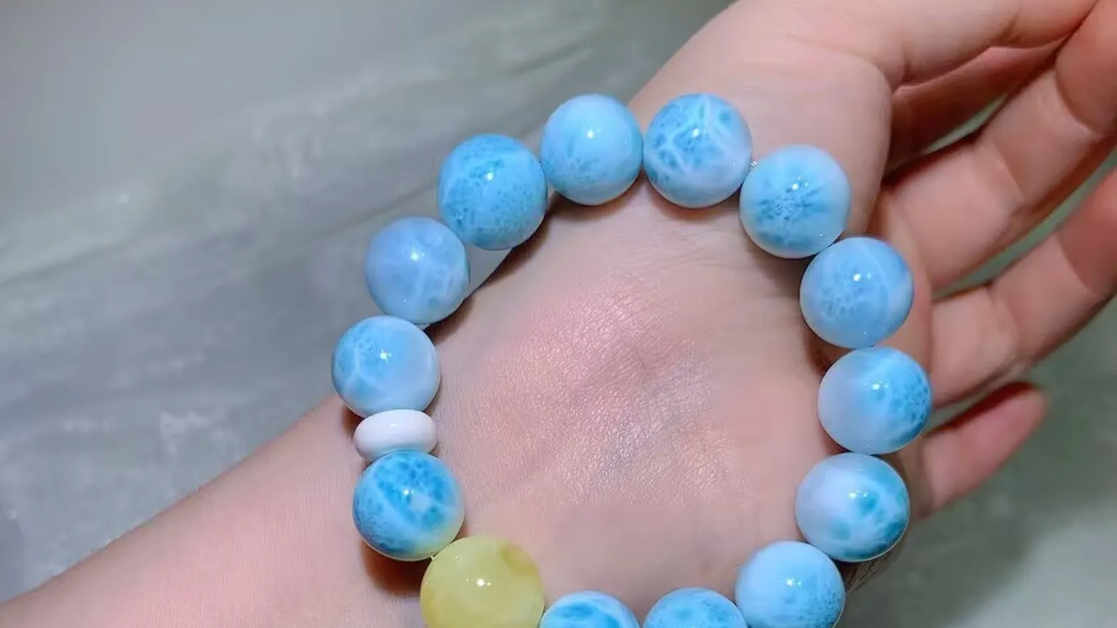一条带白色水波纹的海蓝色海纹石手链戴在手腕上