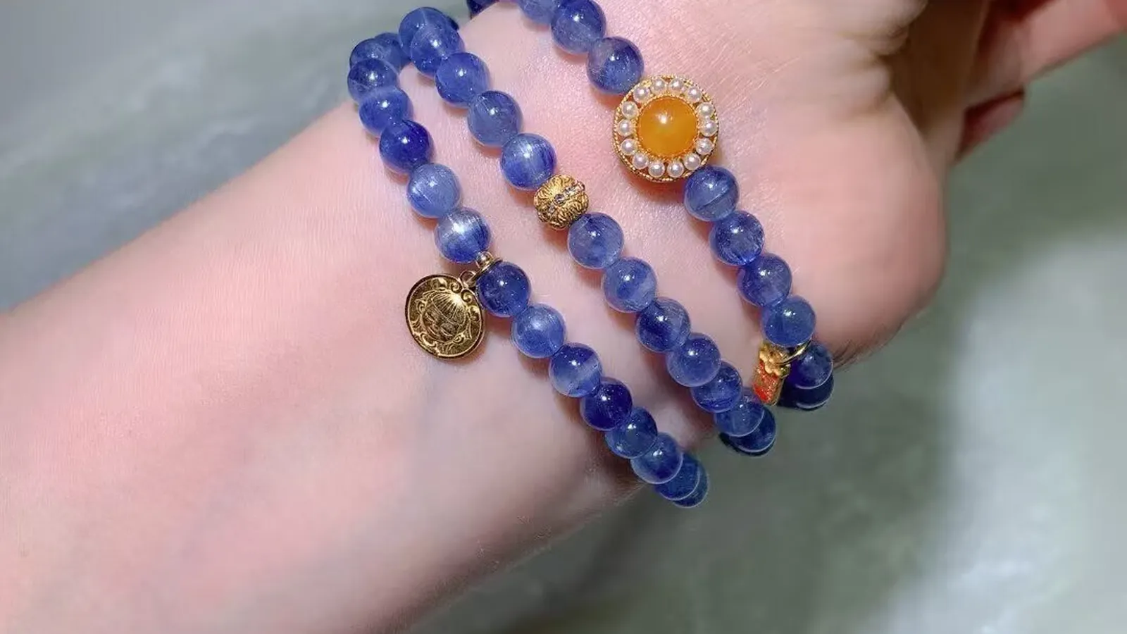 绕在手腕上的天然蓝晶石多圈手链，深浅蓝色条纹珠配蜜黄色蛋面和古法圆牌吊坠