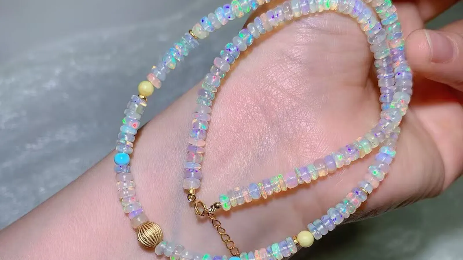 手中的 4.7mm 欧泊串珠项链：闪着彩虹变彩的白色欧泊片珠，配复古风棱纹圆珠和延长链